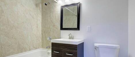 A bathroom with a bathtub, a sink with a mirror above it, and a toilet.