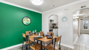 A dining area with a green accent wall, a round mirror, and a view into the kitchen. - Walk to World Cup Games! Walk to AT&T & Globe Life + Small Yard (Arlington)