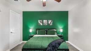 A bedroom with a green wall, a bed with green bedding, two bedside tables with lamps, and a ceiling fan. - Walk to World Cup Games! Walk to AT&T & Globe Life + Small Yard (Arlington)