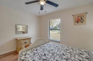 Une chambre à coucher comprenant un lit, une commode, un ventilateur de plafond, une fenêtre avec des stores et un miroir fixé au mur.