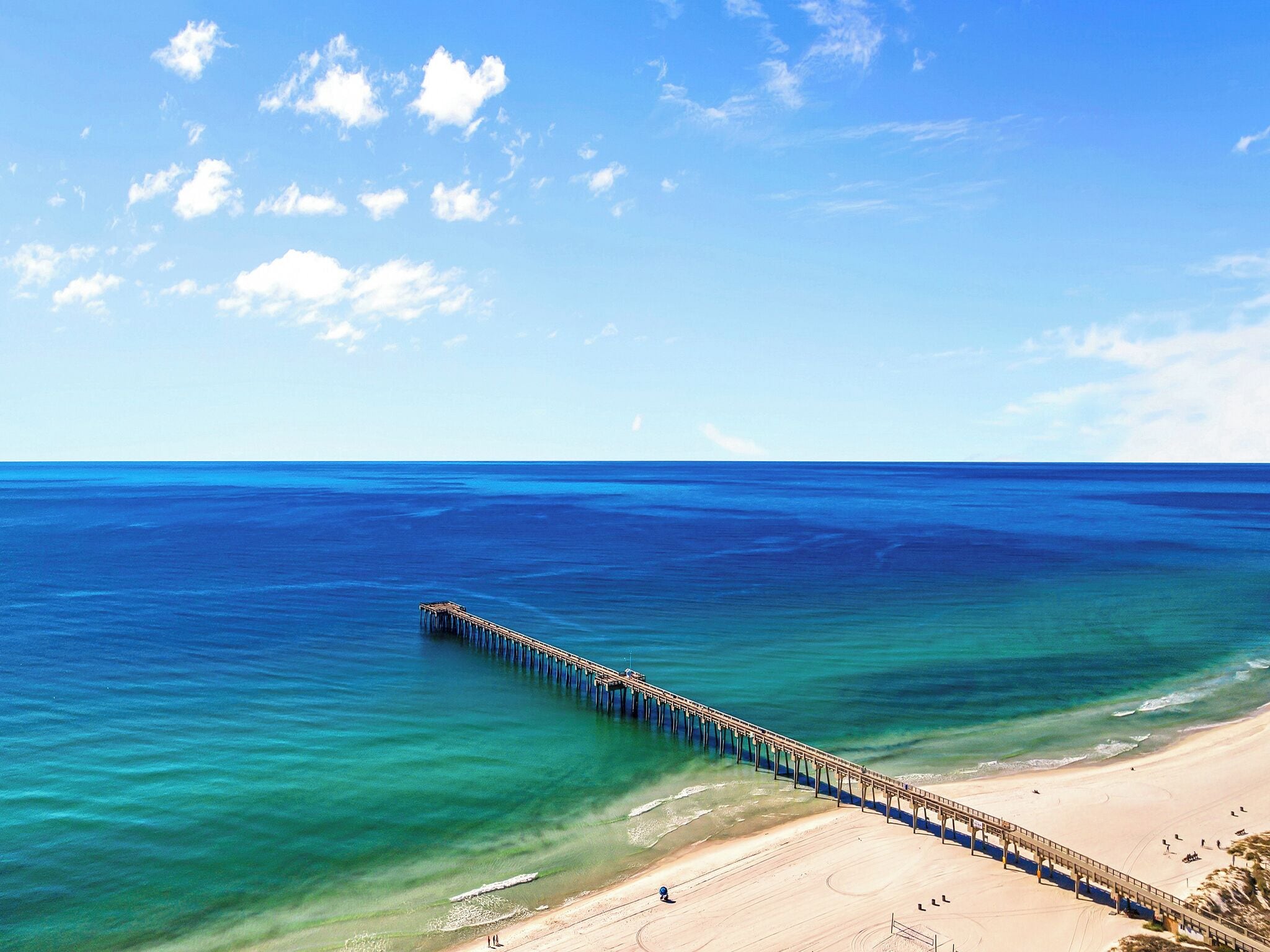 A long pier extending into the ocean with a beach and clear sky.