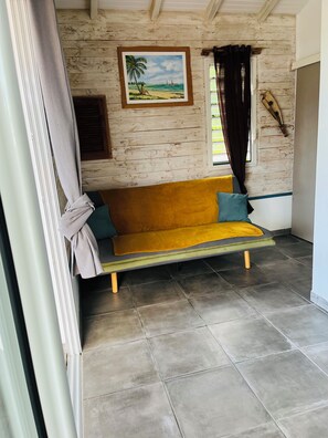 Ein Zimmer mit einer Holzwand, einem Strandbild, einem gelben Sofa und einem Fenster mit Vorhängen.