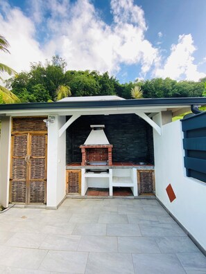 Eine Terrasse mit einem Backofen aus Ziegeln, einem überdachten Sitzbereich und einer weißen Wand mit einem Fenster.