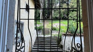 Door een metalen hekwerk is een trap te zien die naar een gebouw met een tuin leidt.