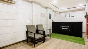Ett väntrum med en svart receptionsdisk märkt med texten ”TOWNHOUSE & Company – serviceavdelning”, två stolar, en grön matta och en vägg med våningsplaner samt en skylt som visar var receptionen finns.