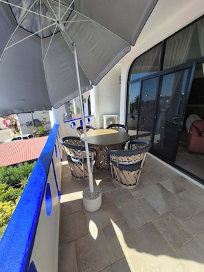 Une terrasse avec une table et des chaises, un parasol et une vue sur l’extérieur.