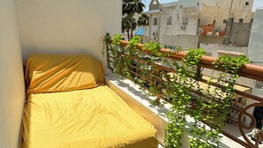 Ein kleiner Balkon mit Bett, Blick auf die Nachbarschaft und einer weißen Wand mit Grünpflanzen.