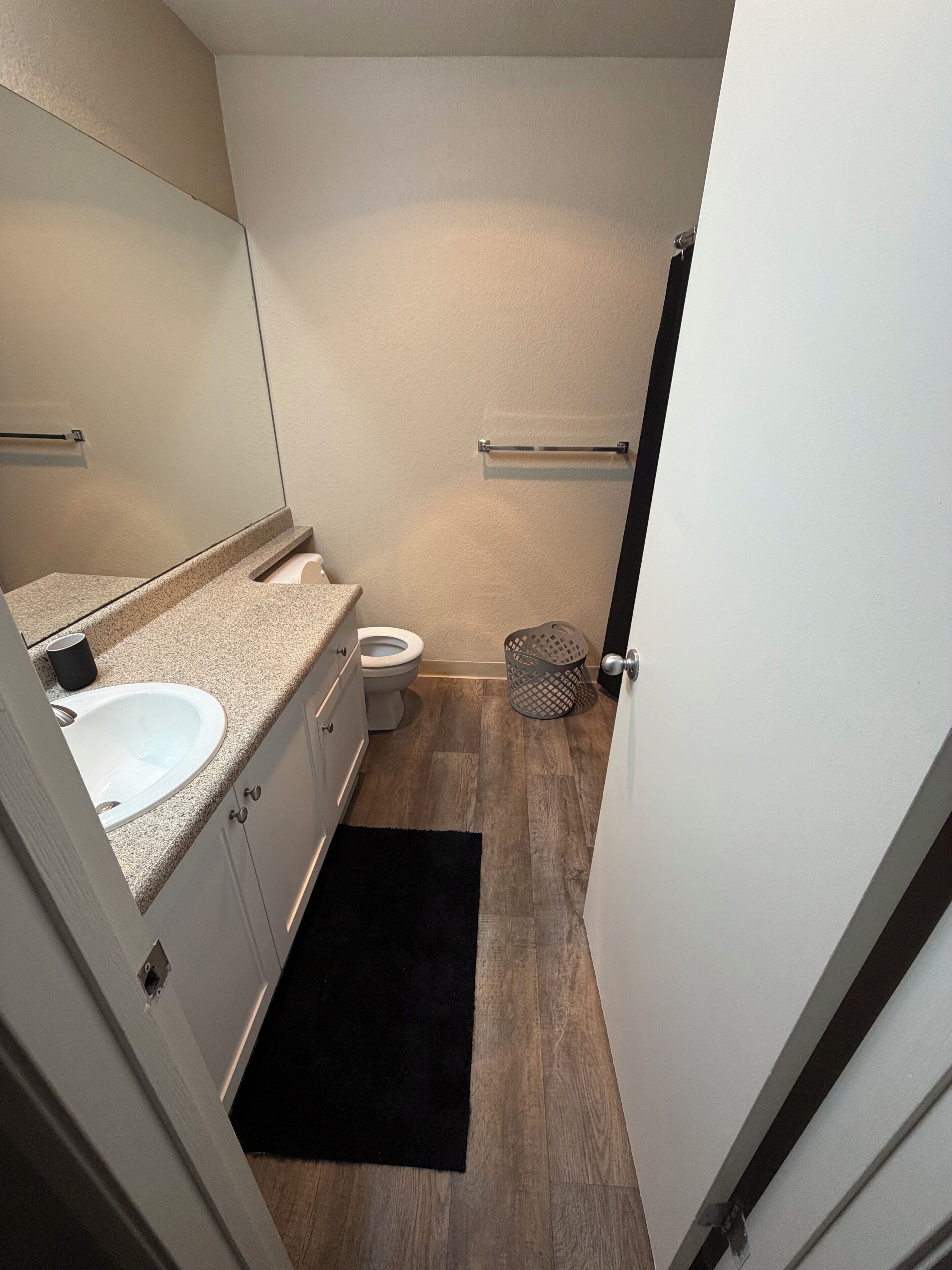 A compact bathroom with a white sink, a toilet, a mirror, and a small trash bin.