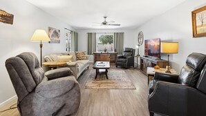 A living room with a sofa, armchair, coffee table, and a TV. - Tranquil Sun City West 2BR | 55+ Community Pool (Sun City West)