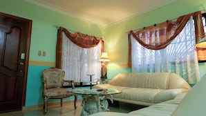 A living room with a sofa, a chair, a table, and curtains. - Large House With AC Wifi Parking Ideal for Families (San Juan de la Maguana)
