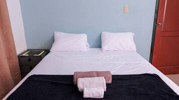 A neatly made bed with white linens, a black blanket, and two towels, a red door, and a light blue wall.