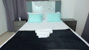 A neatly made bed with a black and white cover, two turquoise pillows, and a white bedside table with a remote control. - Large House With AC Wifi Parking Ideal for Families (San Juan de la Maguana)