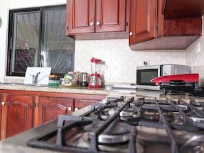 A kitchen with wooden cabinets, a gas stove, a microwave, and a blender on the counter.