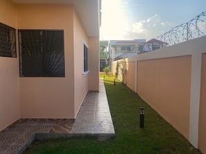 A narrow pathway leading to a building with a tiled floor and a small garden area.