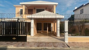 A two-story house with a covered entrance, a gated driveway, and a satellite dish. - Large House With AC Wifi Parking Ideal for Families (San Juan de la Maguana)