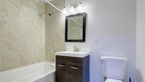 A bathroom with a bathtub, a sink with a mirror above it, and a toilet. - Spacious 4-bedroom house with AC in brilliant Annapolis (Annapolis)