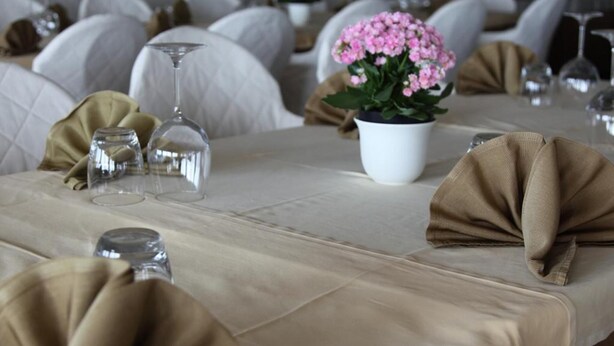 A table set with a white tablecloth, a potted plant, and folded napkins. - Hotel San Carlo (Lignano Sabbiadoro)