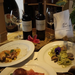 A dining table with two plates of food, two wine bottles, and a menu. - Hotel San Carlo (Lignano Sabbiadoro)