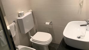 Een kleine badkamer met toilet, hygiëneschuimer en wastafel.