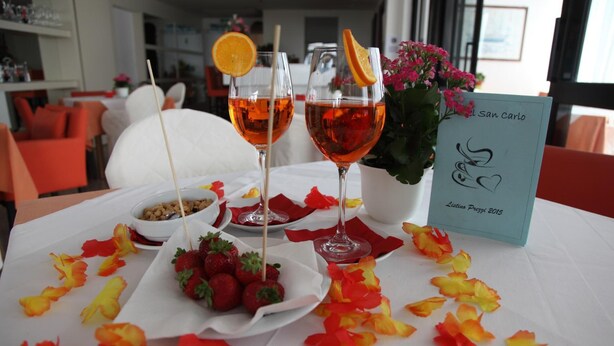Een tafel met twee glazen rode drank, een schaal aardbeien en een bloemstuk.