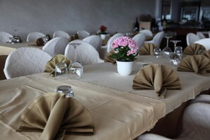 A dining area with tables set for service, white chairs, and a potted plant on the table. - Hotel San Carlo (Lignano Sabbiadoro)