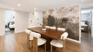 A dining area with a wooden table and chairs, a wall with a nature-themed mural, and a view into another room with a bed. - Free Parking | Walk to Yale & Frank Pepe’s (New Haven)