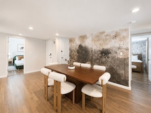 A dining area with a wooden table and chairs, a wall with a nature-themed mural, and a view into another room with a bed. - Free Parking | Walk to Yale & Frank Pepe’s (New Haven)