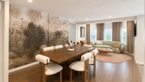A spacious living room with a large wooden dining table surrounded by chairs, a green sofa, and a large wall mural. - Free Parking | Walk to Yale & Frank Pepe’s (New Haven)