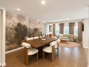 A spacious living room with a large wooden dining table surrounded by chairs, a green sofa, and a large wall mural. - Free Parking | Walk to Yale & Frank Pepe’s (New Haven)