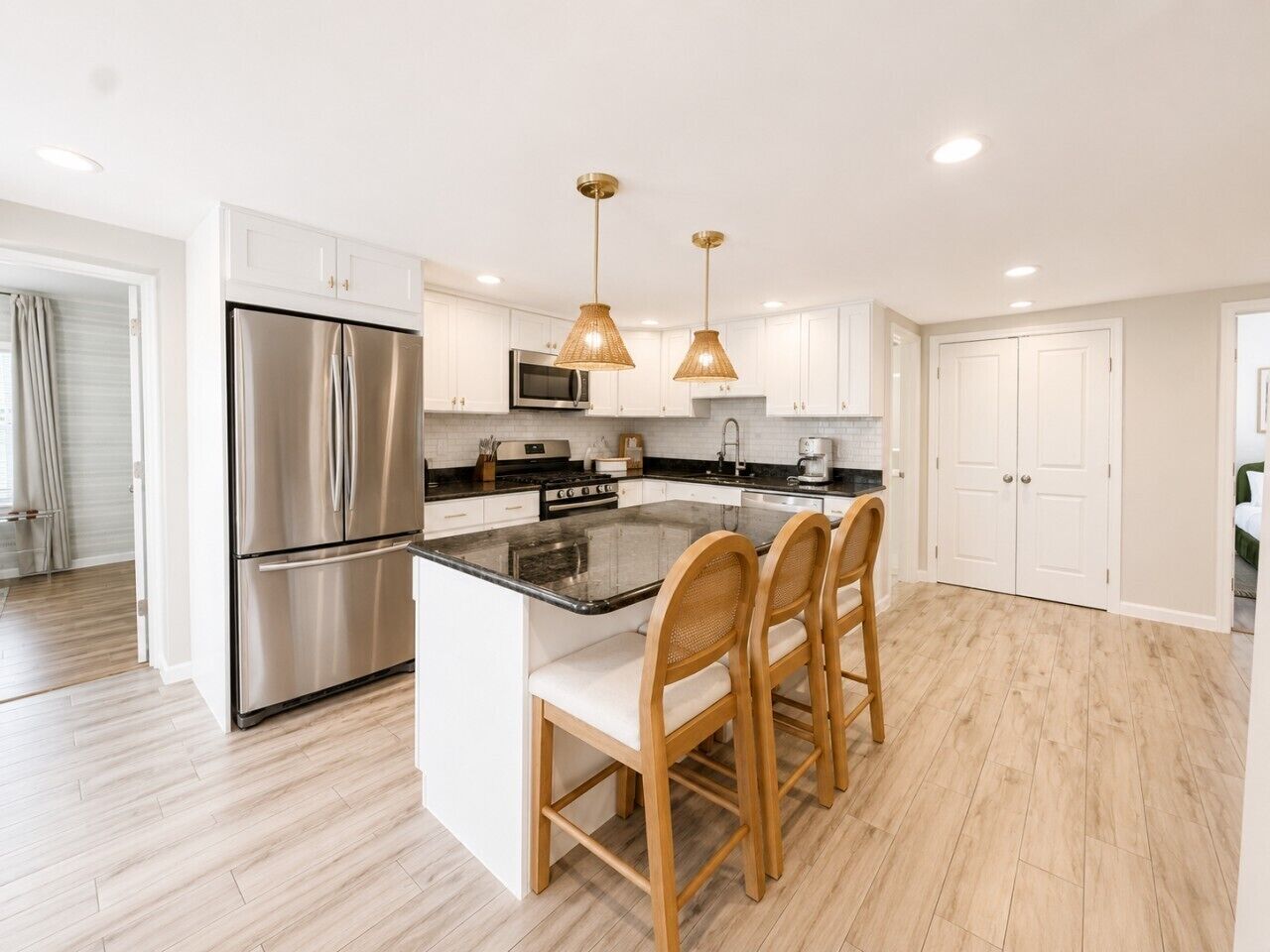A modern kitchen with a stainless steel refrigerator, a microwave, and a built-in oven. There are two wooden chairs at the island counter, and pendant lights hang above.