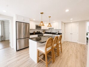 A modern kitchen with a stainless steel refrigerator, a microwave, and a built-in oven. There are two wooden chairs at the island counter, and pendant lights hang above. - Free Parking | Walk to Yale & Frank Pepe’s (New Haven)