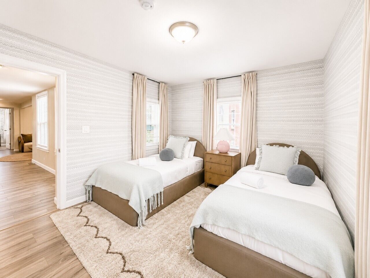 A bedroom with two beds, a nightstand, and a window with curtains.