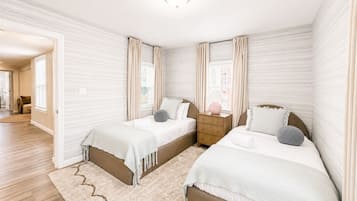 A bedroom with two beds, a nightstand, and a window with curtains.
