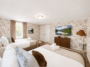 Ein Hotelzimmer mit zwei Betten, einem Kleiderschrank, einem Fernseher und einem Bild an der Wand.