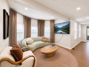 Ein modernes Wohnzimmer mit einer gebogenen Couch, einem runden Couchtisch und einem großen Flachbildfernseher, der an der Wand befestigt ist.