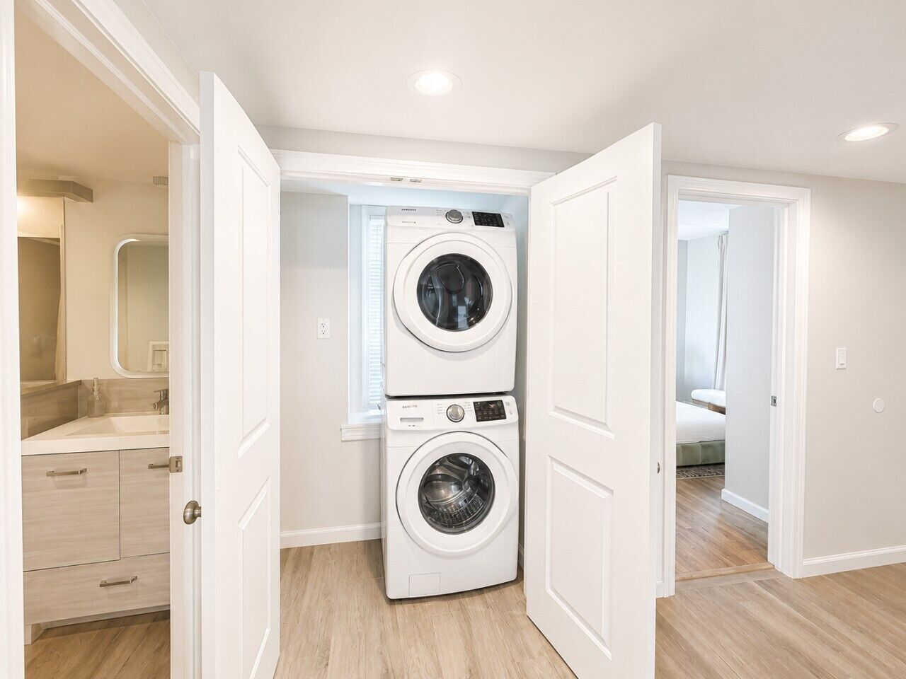 A laundry room with two stacked washing machines, a wooden floor, and white walls.