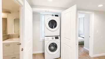 A laundry room with two stacked washing machines, a wooden floor, and white walls.