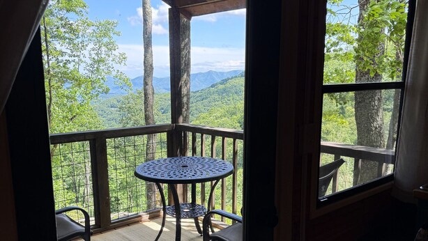 A balcony with a table and chairs, a view of a forested mountain range, and a wooden ceiling structure. - Trailblazer - Cabin w Mtn Views (Black Mountain)
