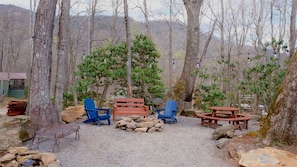 Un espace extérieur aménagé dans un style rustique, avec des bancs et des chaises en bois, entouré d’arbres et recouvert d’un sol de gravier.