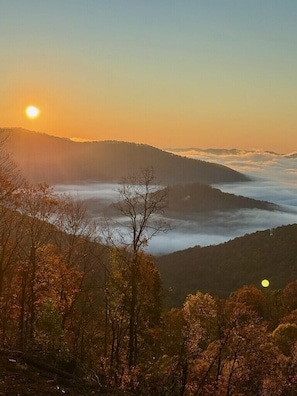 Un paysage montagneux avec un lever ou un coucher de soleil, des arbres et un ciel dégagé.