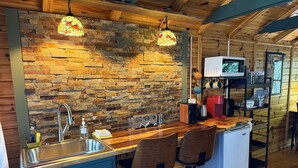 A rustic kitchen with a stone wall backsplash, wooden bar stools, a sink, and a microwave. - Trailblazer - Cabin w Mtn Views (Black Mountain)