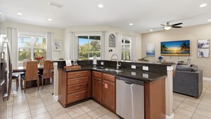 A modern kitchen with a built-in dishwasher, wooden cabinets, and a dining area with a table and chairs. - WOW! 6BR Pool Villa w/ Game Room Near Disney (Kissimmee)