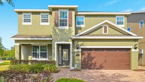 A two-story residential building with a front entrance, a garage, and a landscaped front yard. - WOW! 6BR Pool Villa w/ Game Room Near Disney (Kissimmee)