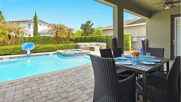 A swimming pool with a basketball hoop, outdoor dining area with wicker chairs, and a view of a residential neighborhood. - WOW! 6BR Pool Villa w/ Game Room Near Disney (Kissimmee)