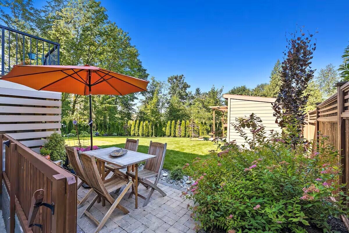 A patio with a table and chairs, a wooden fence, and a garden with various plants.