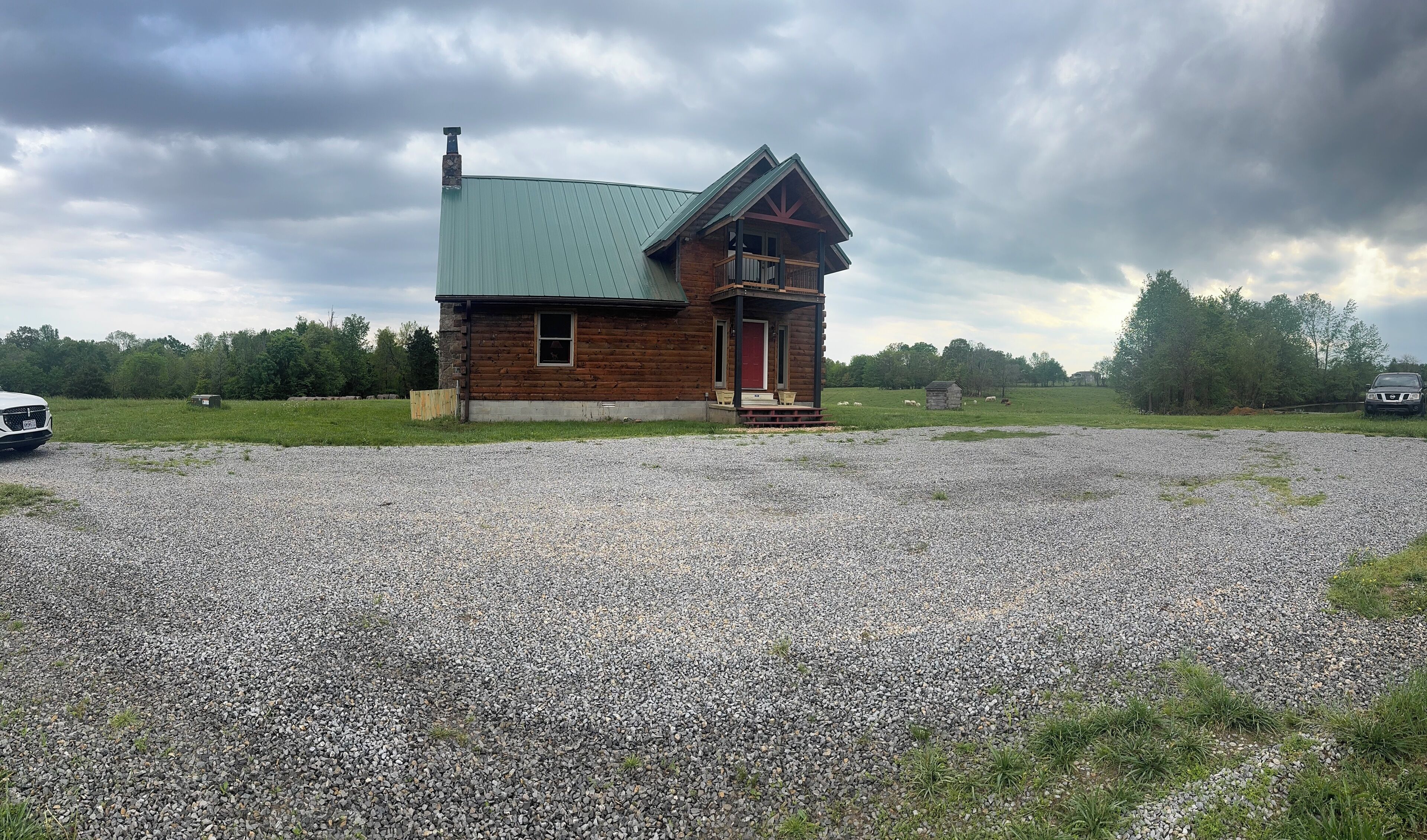 Une cabane rustique avec un toit en métal vert, une véranda en bois et une allée gravillonnée.