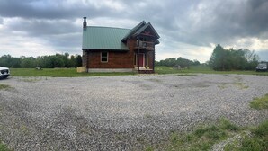 A rustic cabin with a green metal roof, a wooden porch, and a gravel driveway.