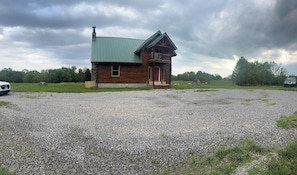 A rustic cabin with a green metal roof, a wooden porch, and a gravel driveway. - Eden’s Rest – Cozy 2BR Cabin in the Woods (Poplar Bluff)