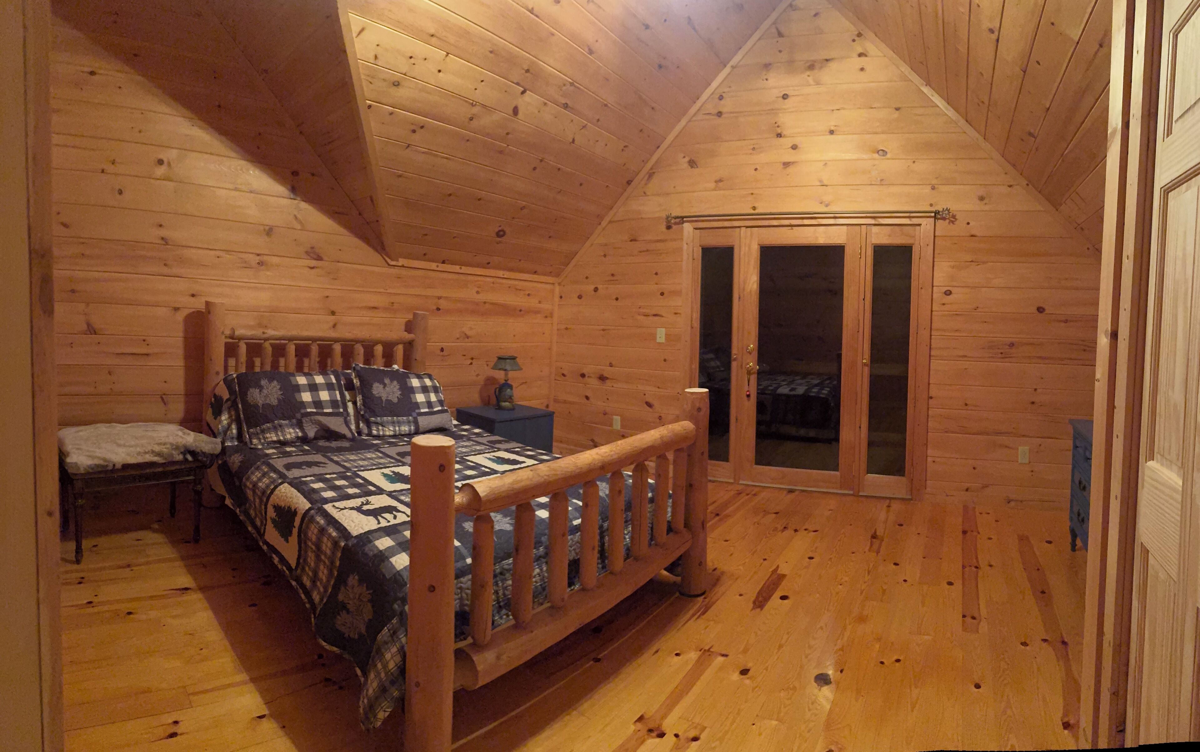 Une chambre située dans une cabane en bois, comprenant un lit, une chaise, une table de chevet et une porte-fenêtre coulissante donnant sur un balcon.