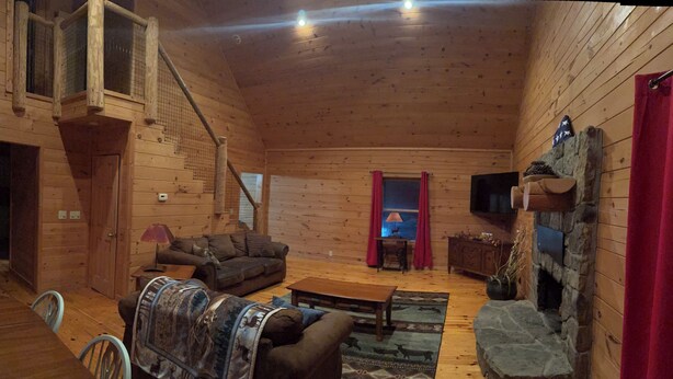 A log cabin interior with a wooden staircase, a fireplace, a sofa, a coffee table, and a television.